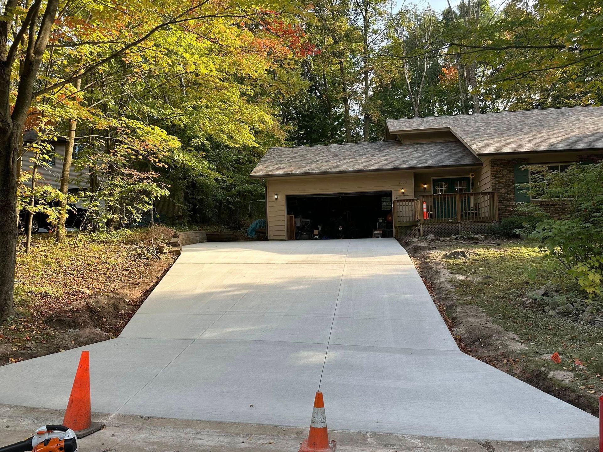Newly poured concrete driveway leading to a garage with a house in the background. Orange traffic cones flank the drive.