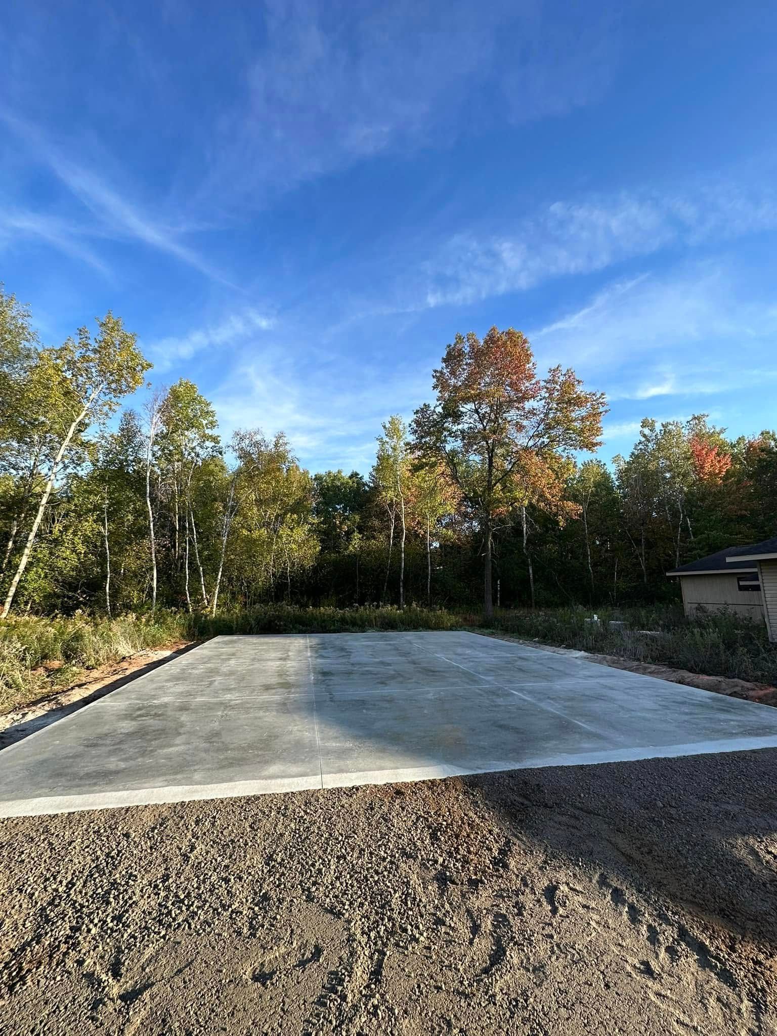 Concrete pad surrounded by gravel, trees, and blue sky.