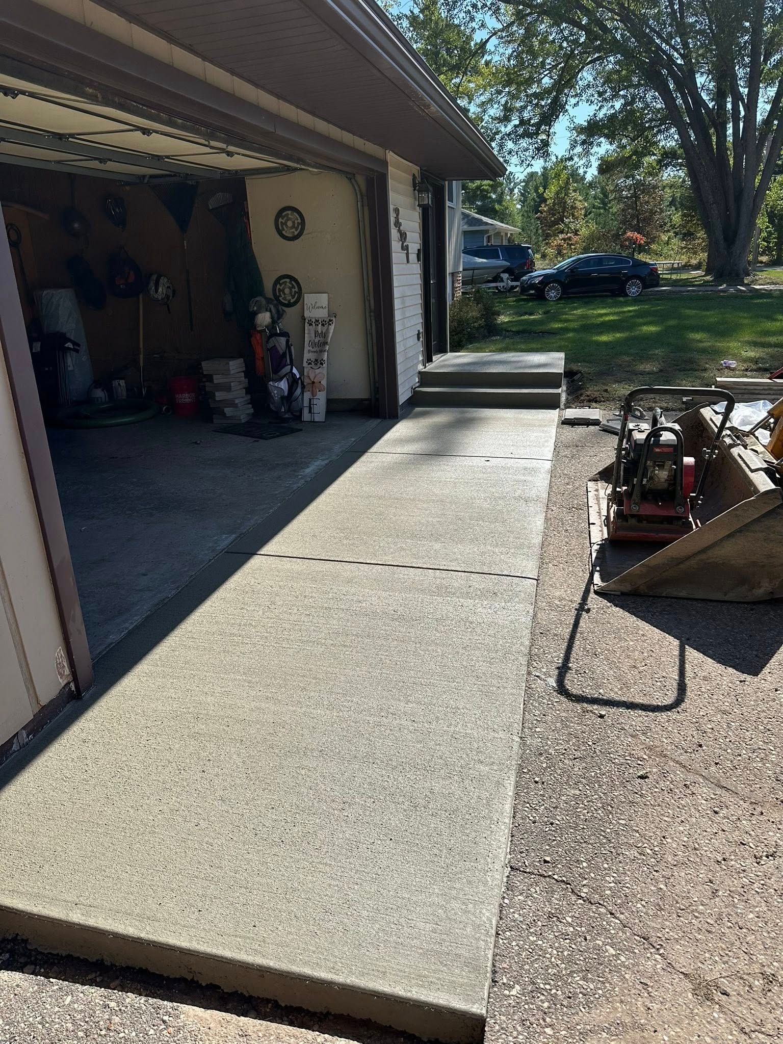 Concrete walkway leading from garage to driveway with gravel and machinery on the right.