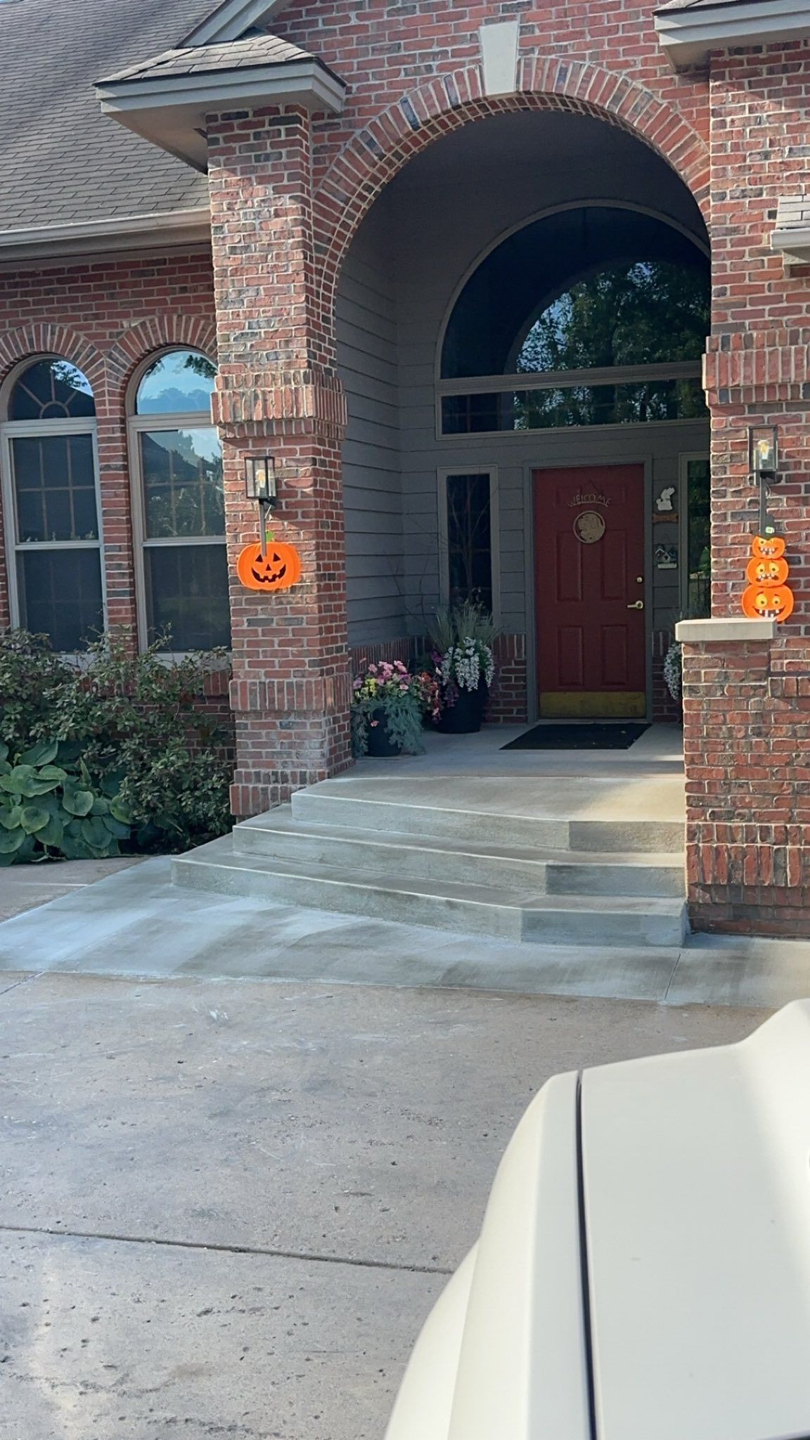 Brick house entrance with pumpkin decorations. Steps lead to a red door under an arch.