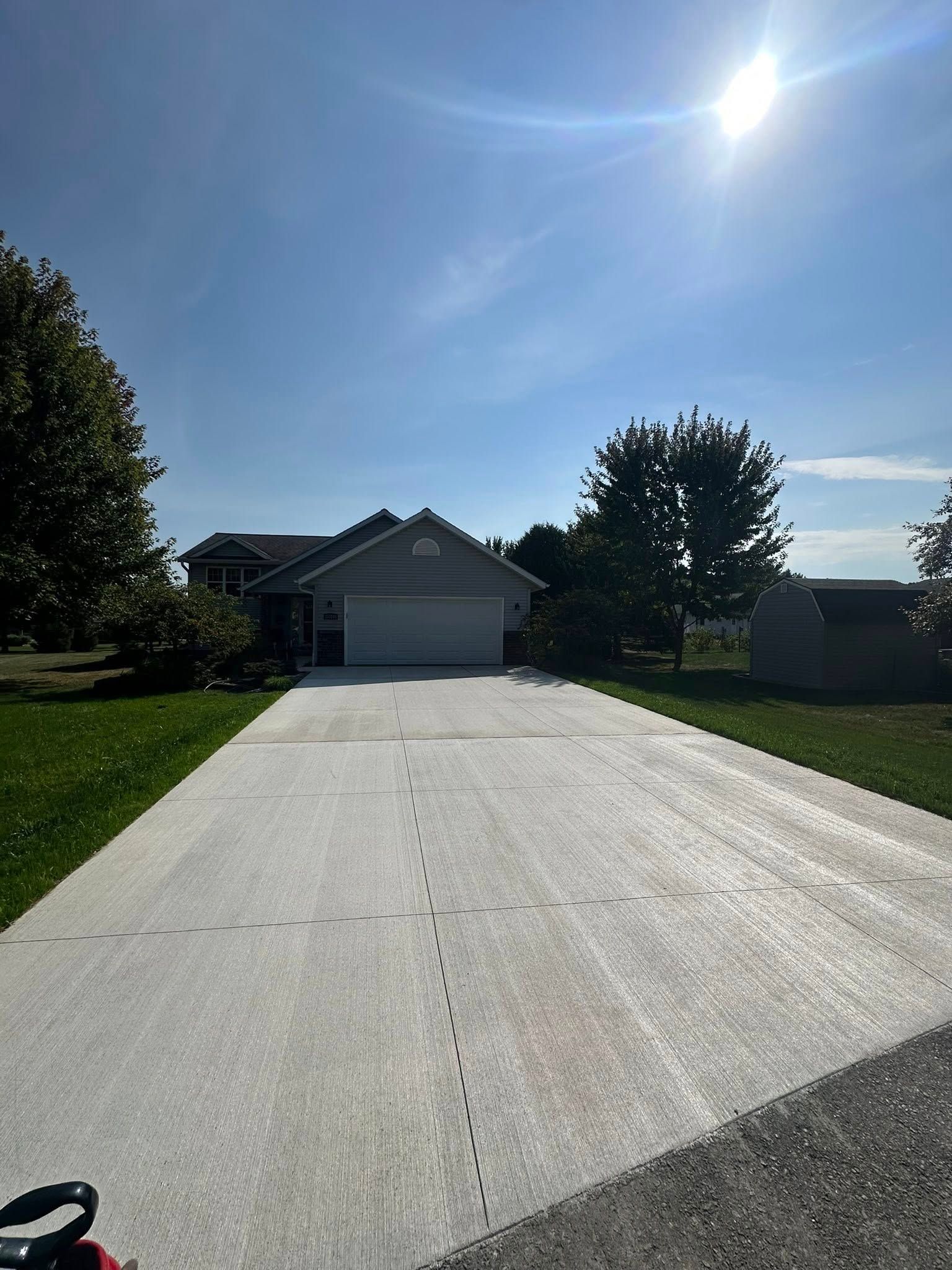 Driveway leading to a light grey house with a two-car garage under a bright sun.