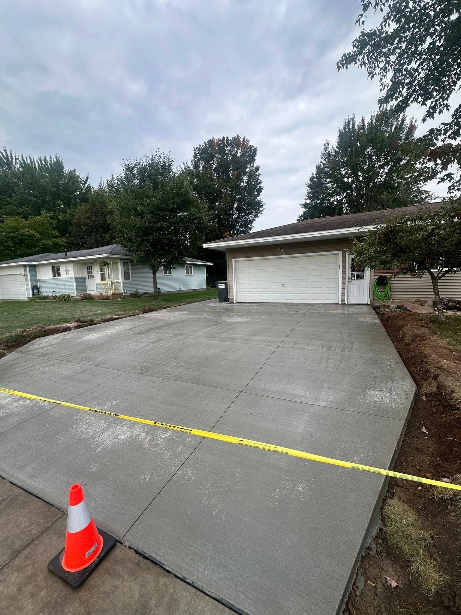 Freshly poured concrete driveway in front of a house, with caution tape and a traffic cone.
