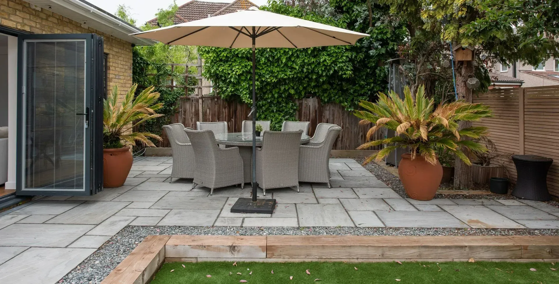 Patio with outdoor dining set under umbrella, potted plants, and green grass.