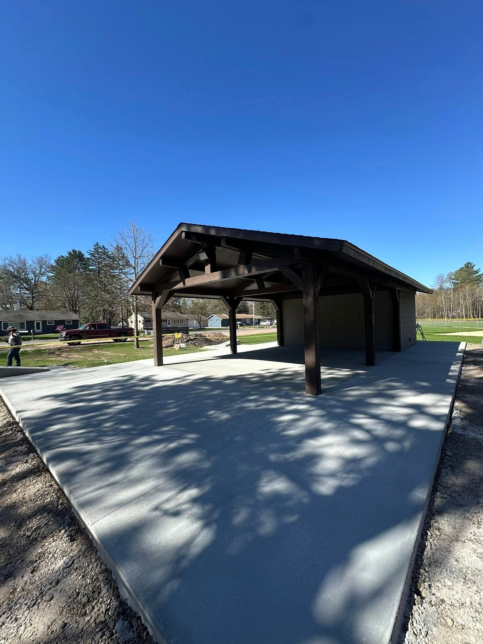 Pavilion with brown roof and posts on concrete slab, blue sky background.