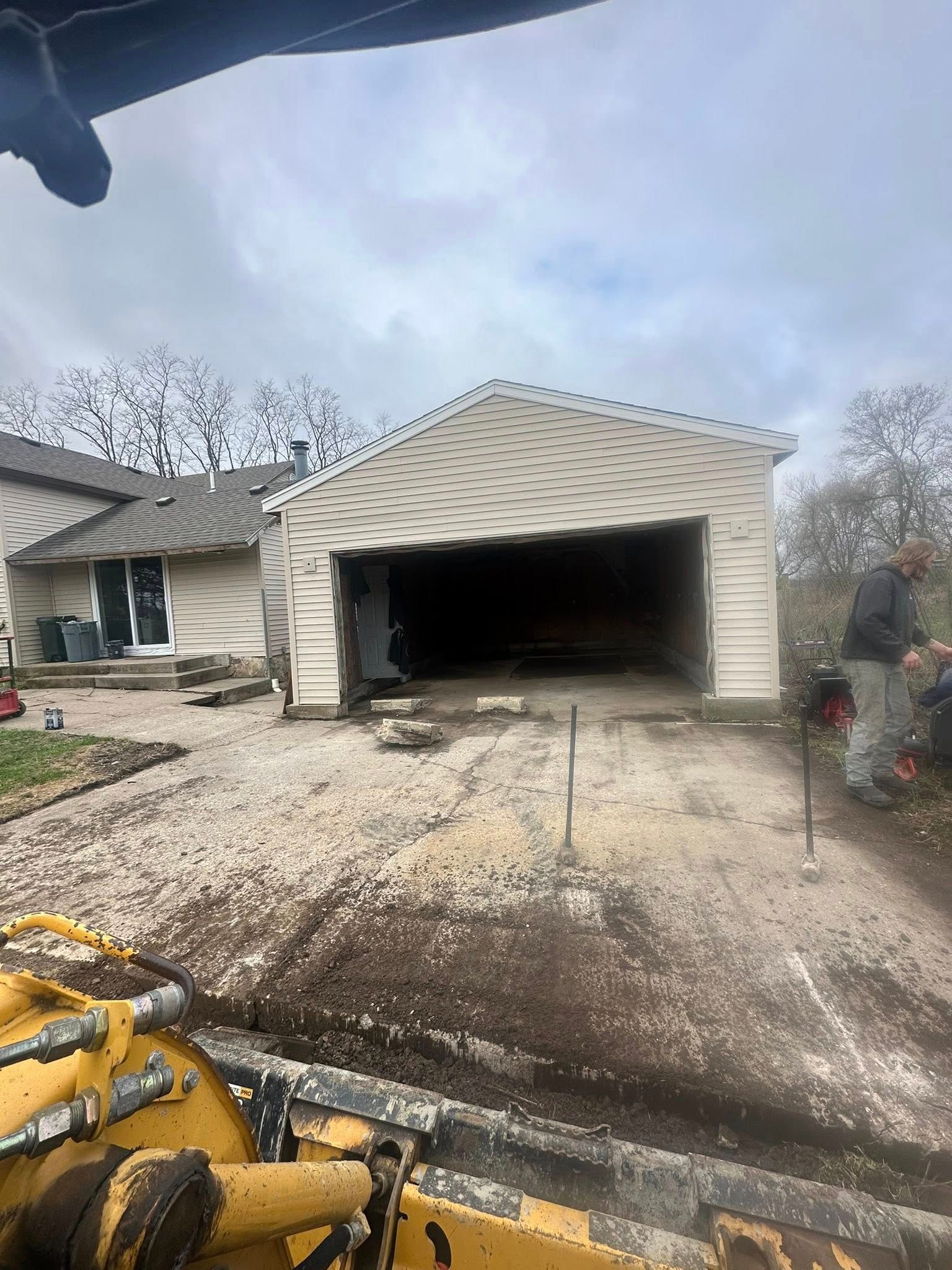 Garage under construction, partially demolished. Dirt driveway in foreground; house in background.