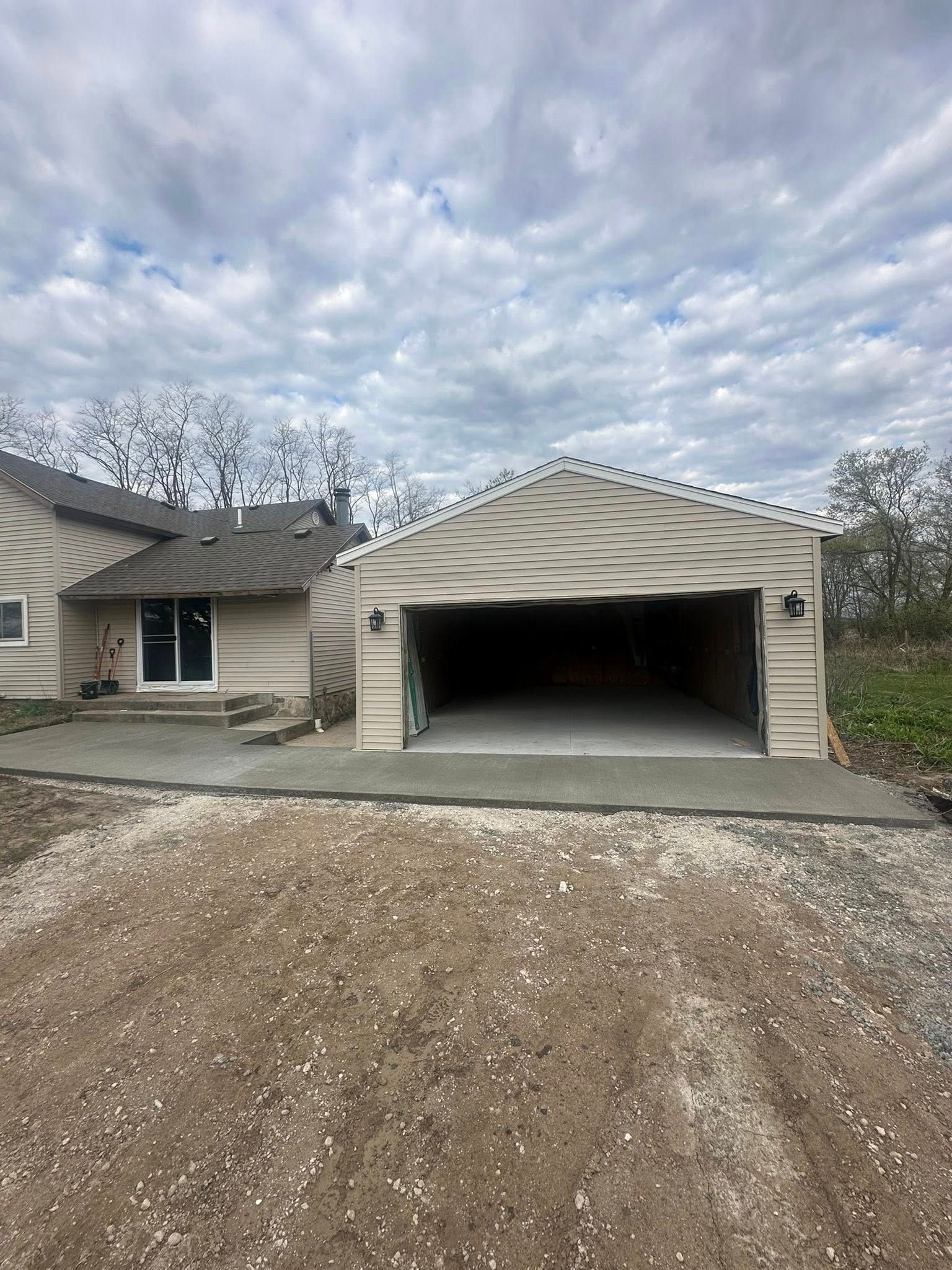 Newly constructed garage with an open door next to a house. Gray gravel driveway.