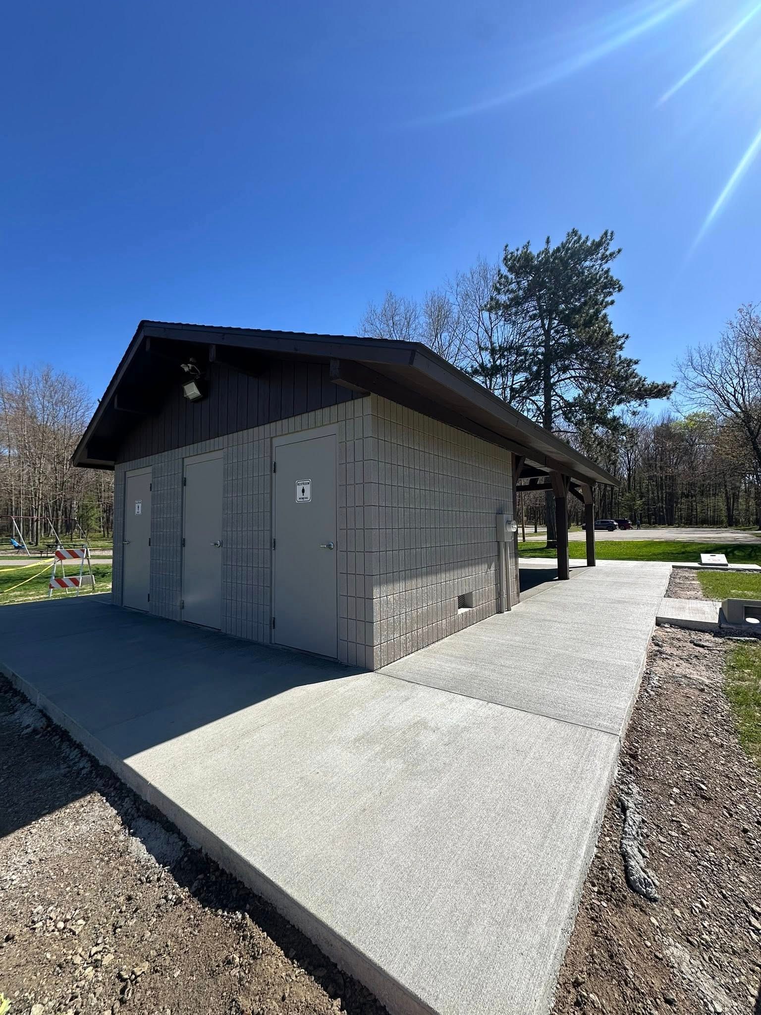 Public restroom building with concrete sidewalk and brown roof under a bright blue sky.