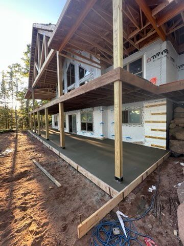Construction site with a concrete patio under a wooden deck and house.