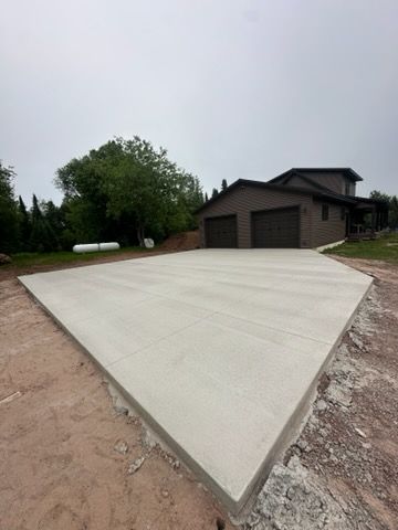 Concrete truck pouring cement on a driveway in front of a house under construction.