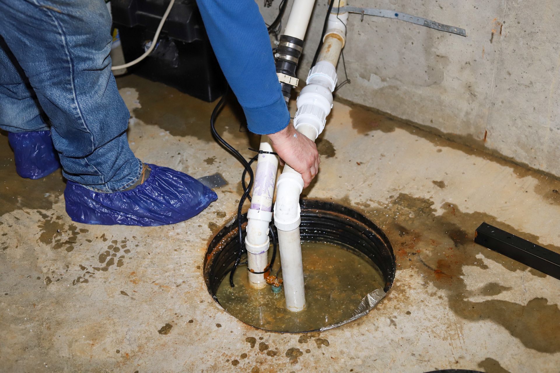 Person working on white PVC pipes in a concrete floor opening with standing water nearby