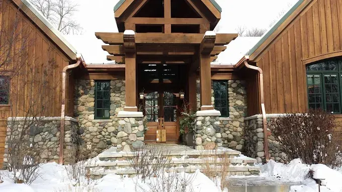 Wooden lodge entrance with stone base and snow. Trellis overhangs doorway.