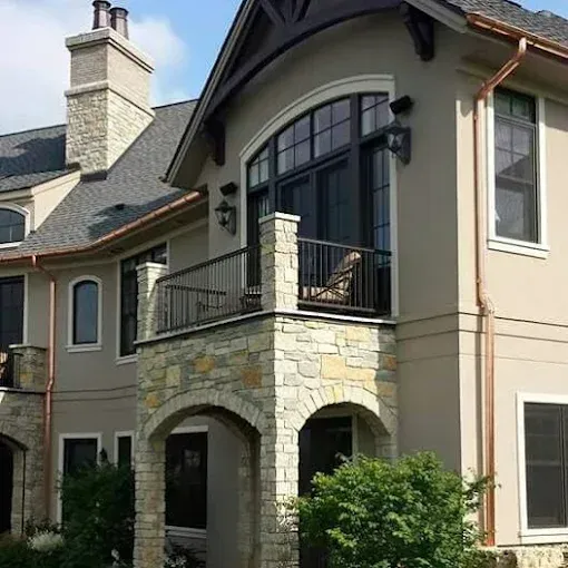 Beige stucco house with stone accents, balcony, and dark-framed windows.