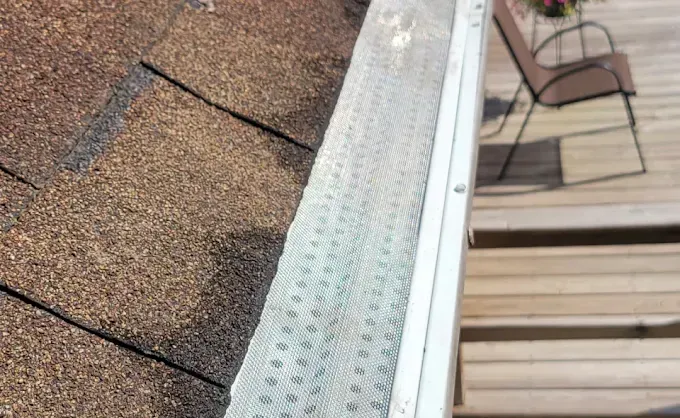 Gutter with mesh cover on a roof next to a wooden deck with chair.