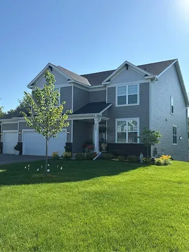 Gray two-story house with white trim, three-car garage, and lush green lawn on a sunny day.
