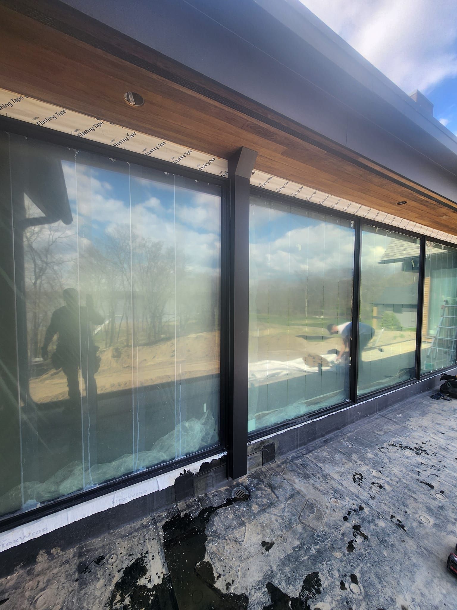 Exterior view of modern building with large glass windows reflecting a cloudy sky and trees.
