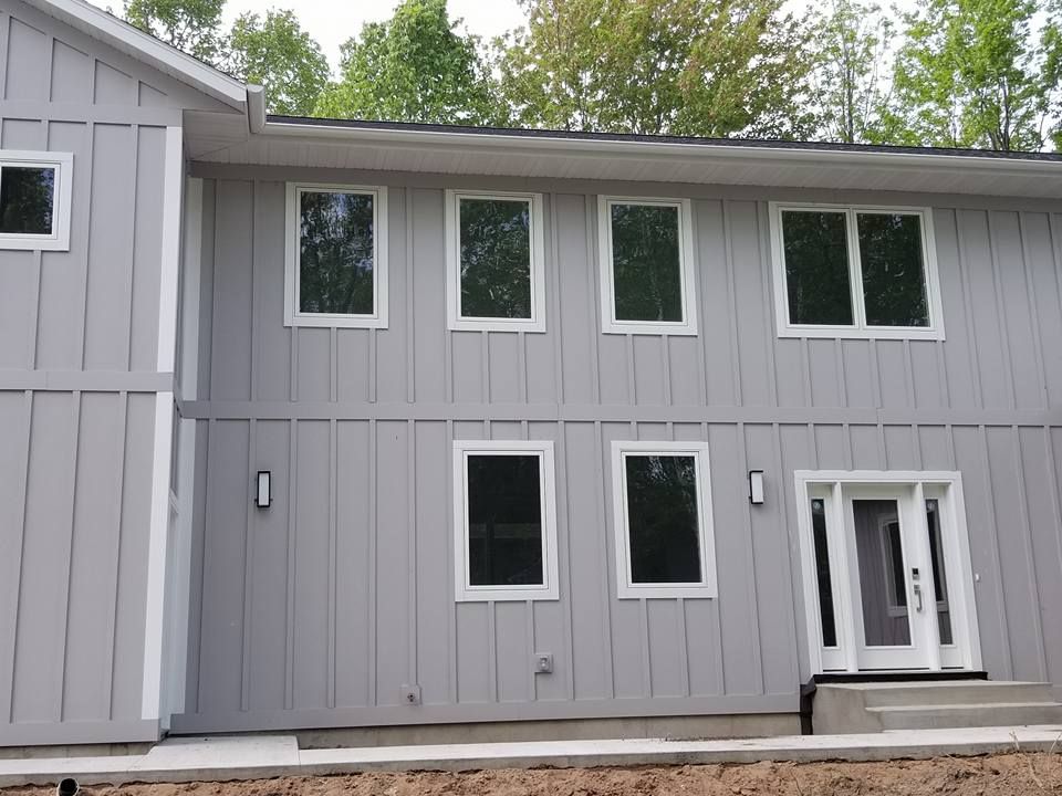 Gray house with white-framed windows and door. Trees in the background.