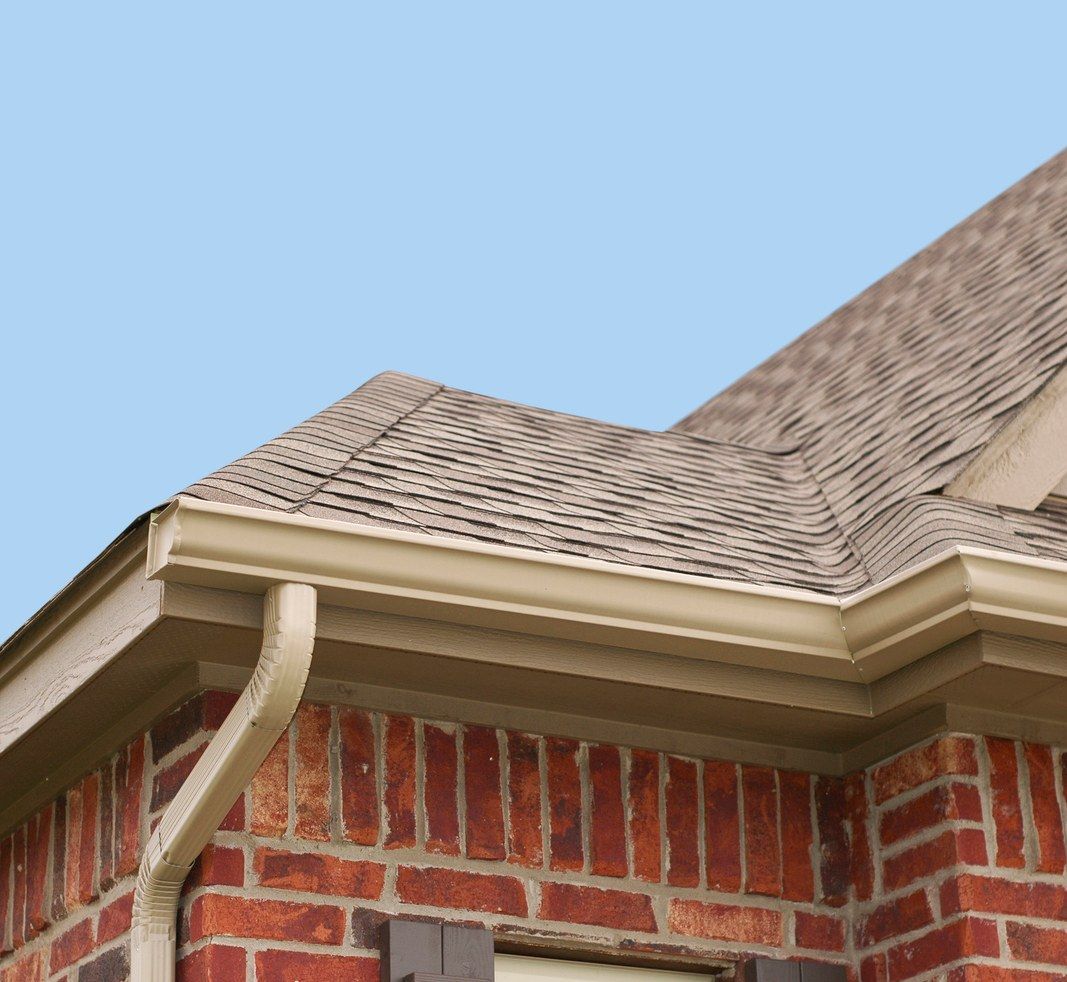 Red brick house with tan gutters, brown roof, and blue sky.