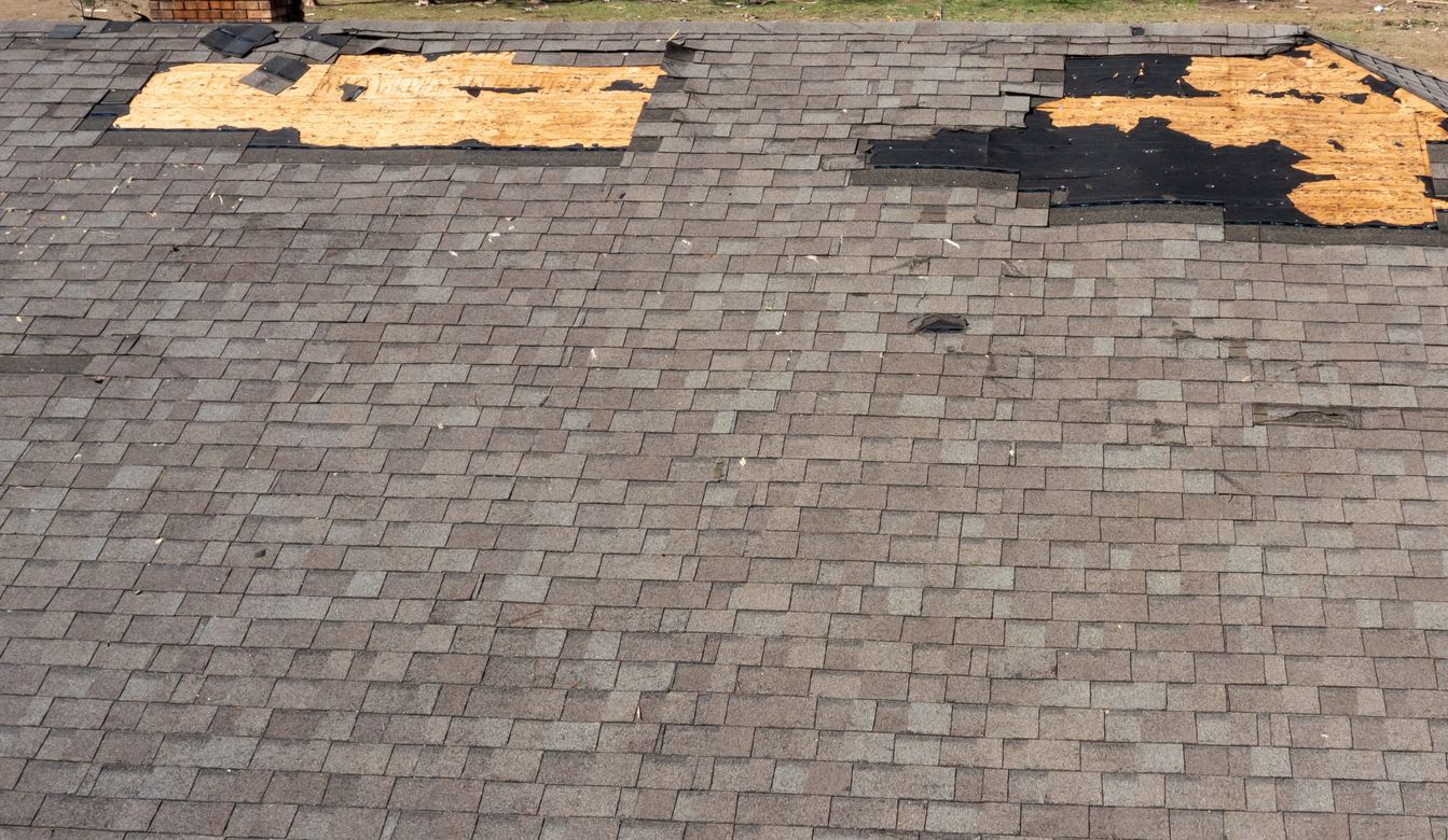 Damaged asphalt shingle roof with missing sections, exposing wooden sheathing.
