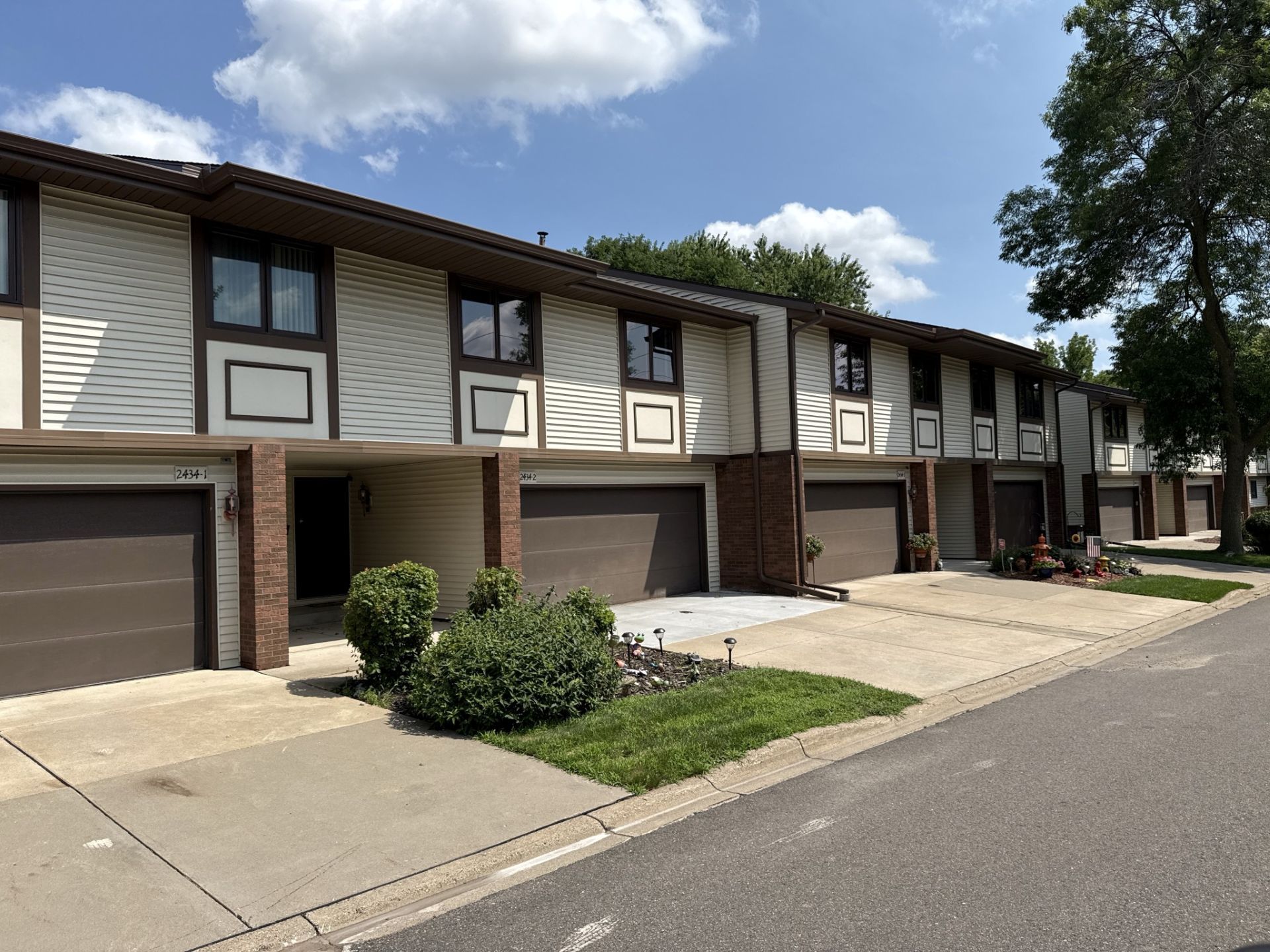 Row of townhouses with brown garage doors, beige siding, and brown trim under a blue sky.