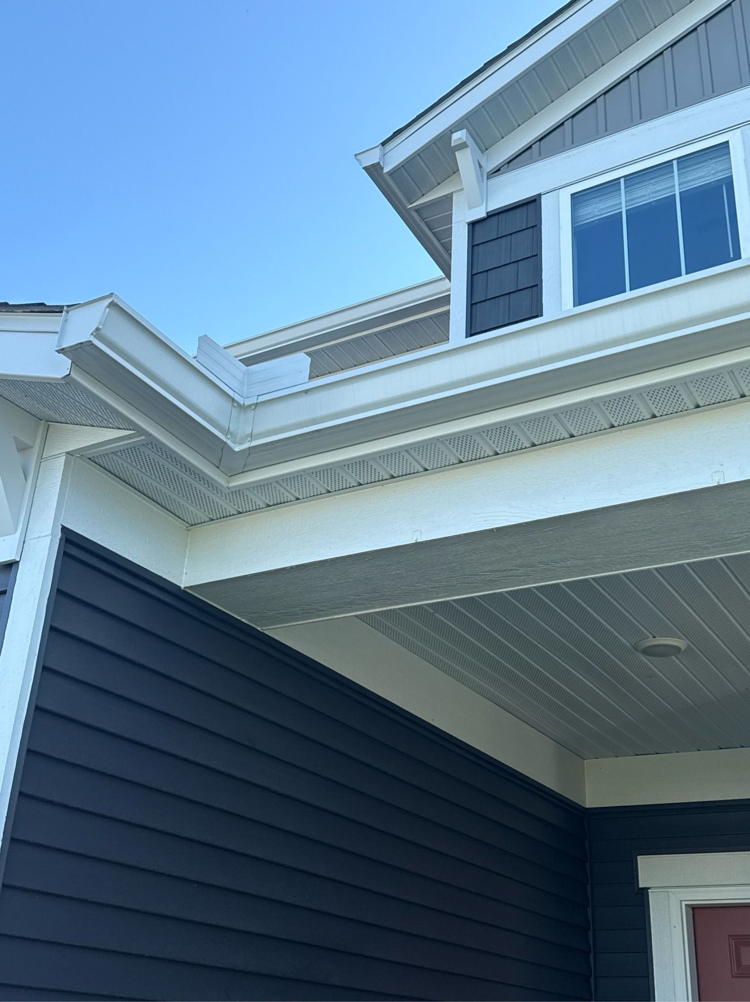 White gutters and trim on a house with blue siding, under a clear, blue sky.