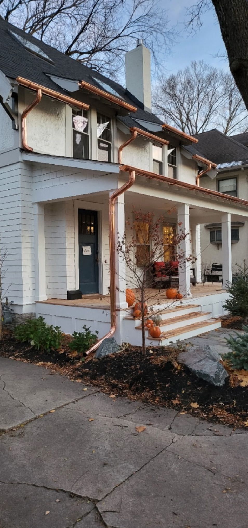 White house with copper gutters, blue door, and porch decorated with pumpkins.