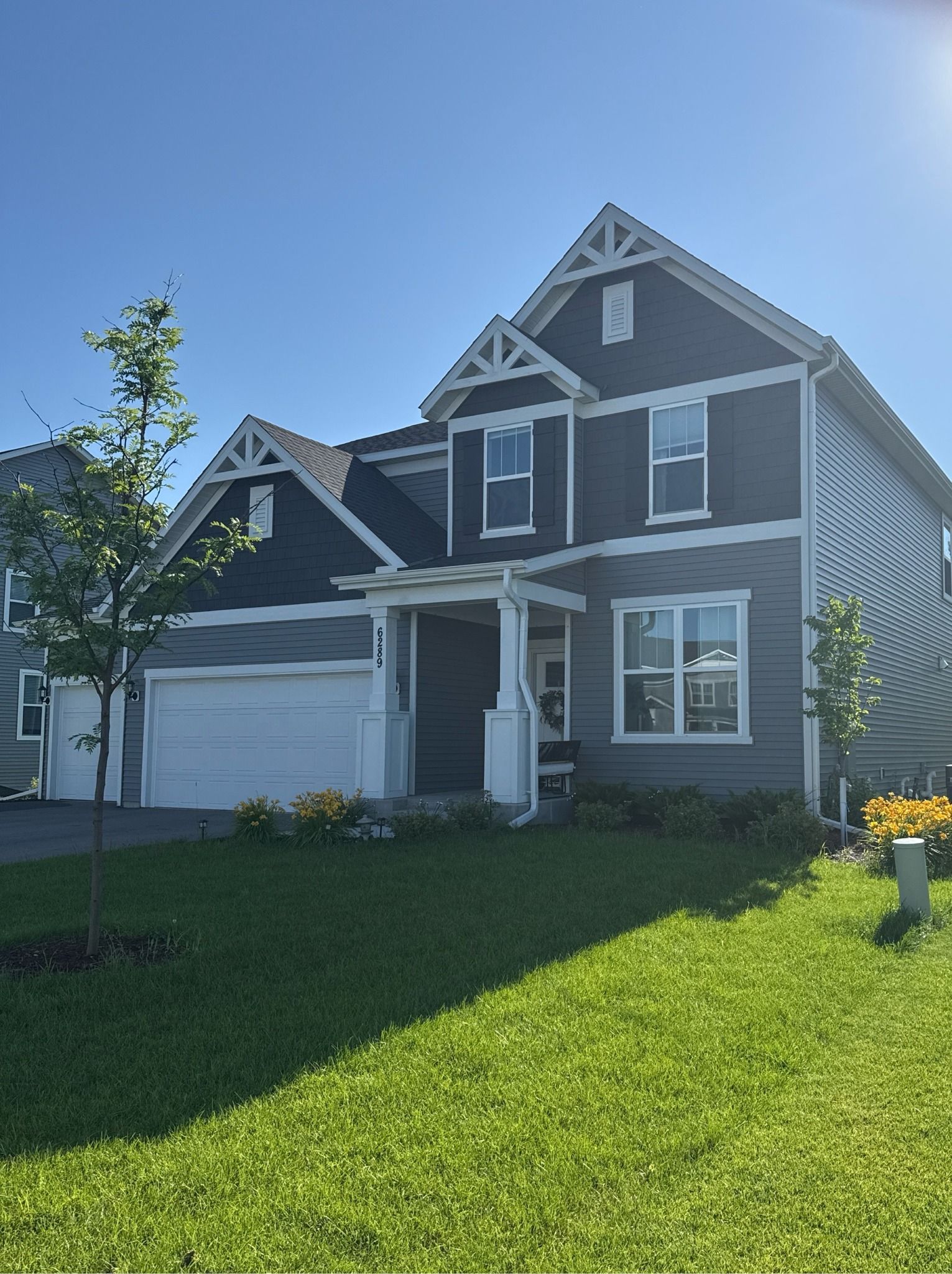 Two-story gray house with white trim, garage, and green lawn under a blue sky.
