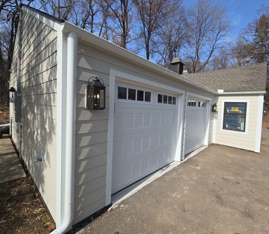 Two-car garage with white doors, tan siding, and black lantern lights.