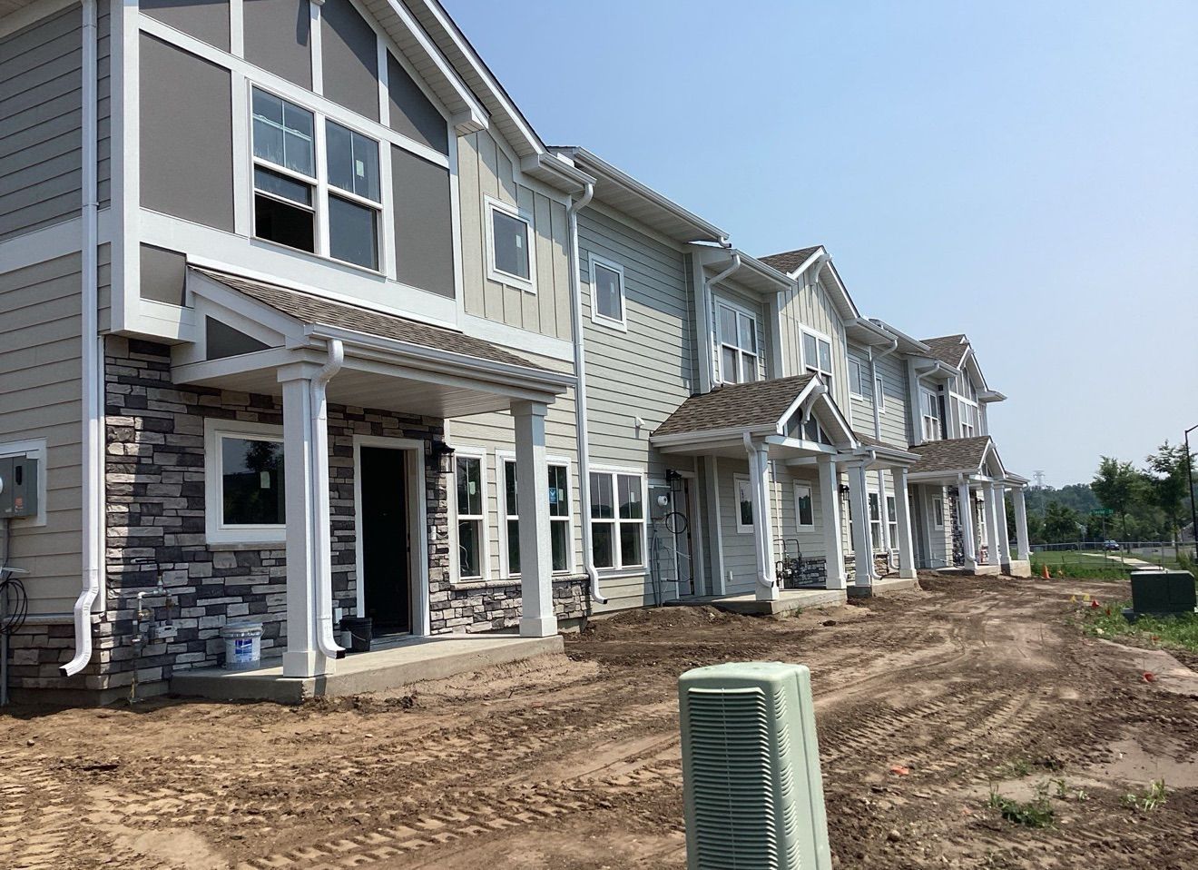Row of newly constructed townhomes with varying gray and stone facades under a sunny sky.