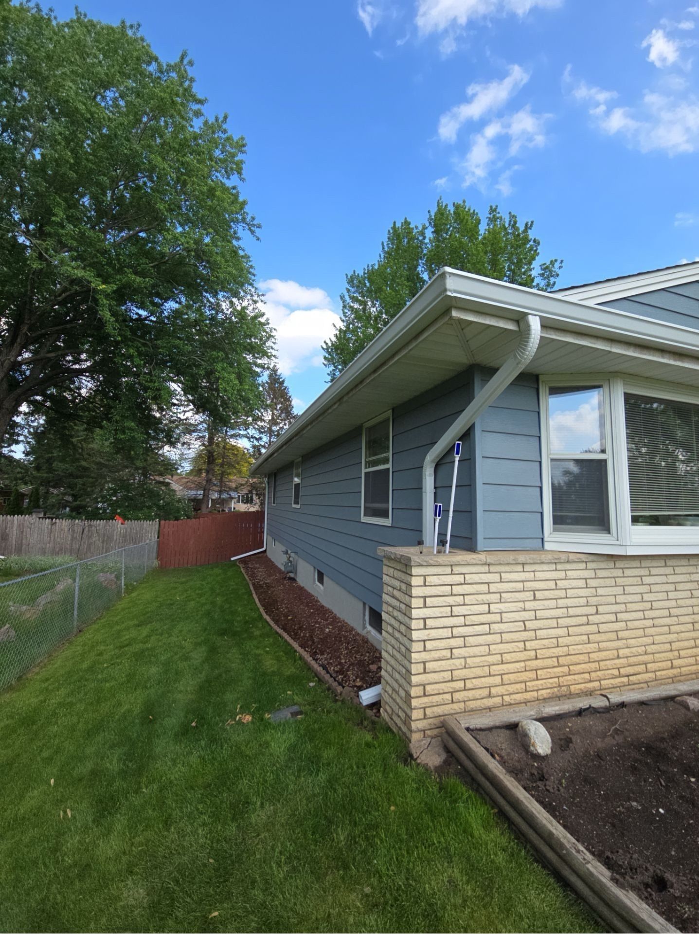 Blue house with white trim and gutters, green lawn, red fence, and bright blue sky.