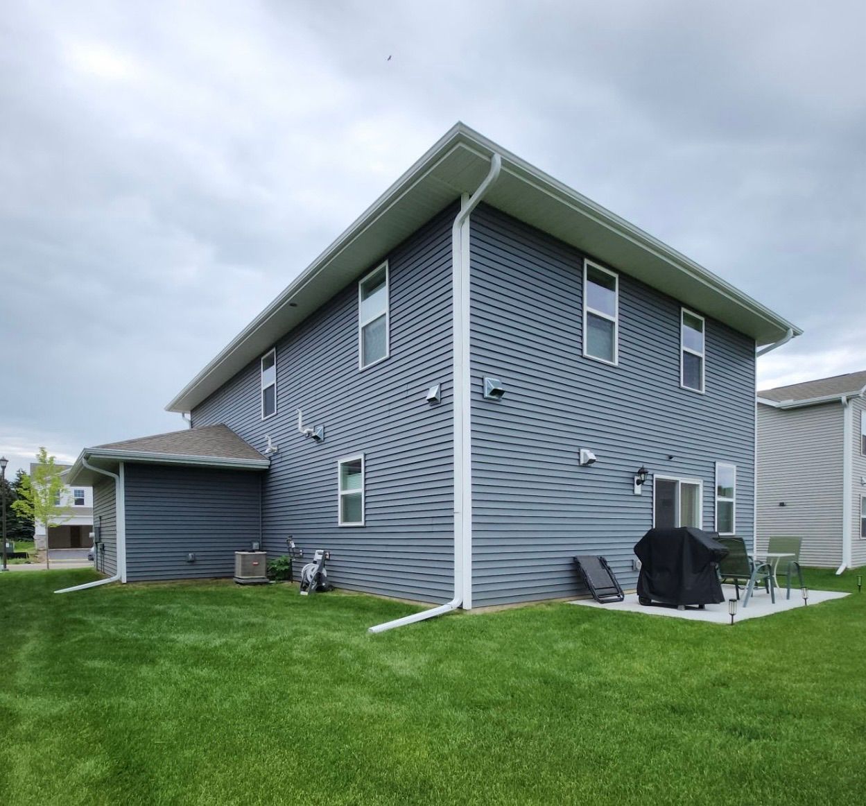 Two-story blue house with green lawn, patio, and cloudy sky.