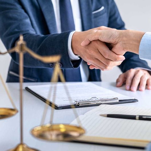 Two men are shaking hands in front of a scale of justice.