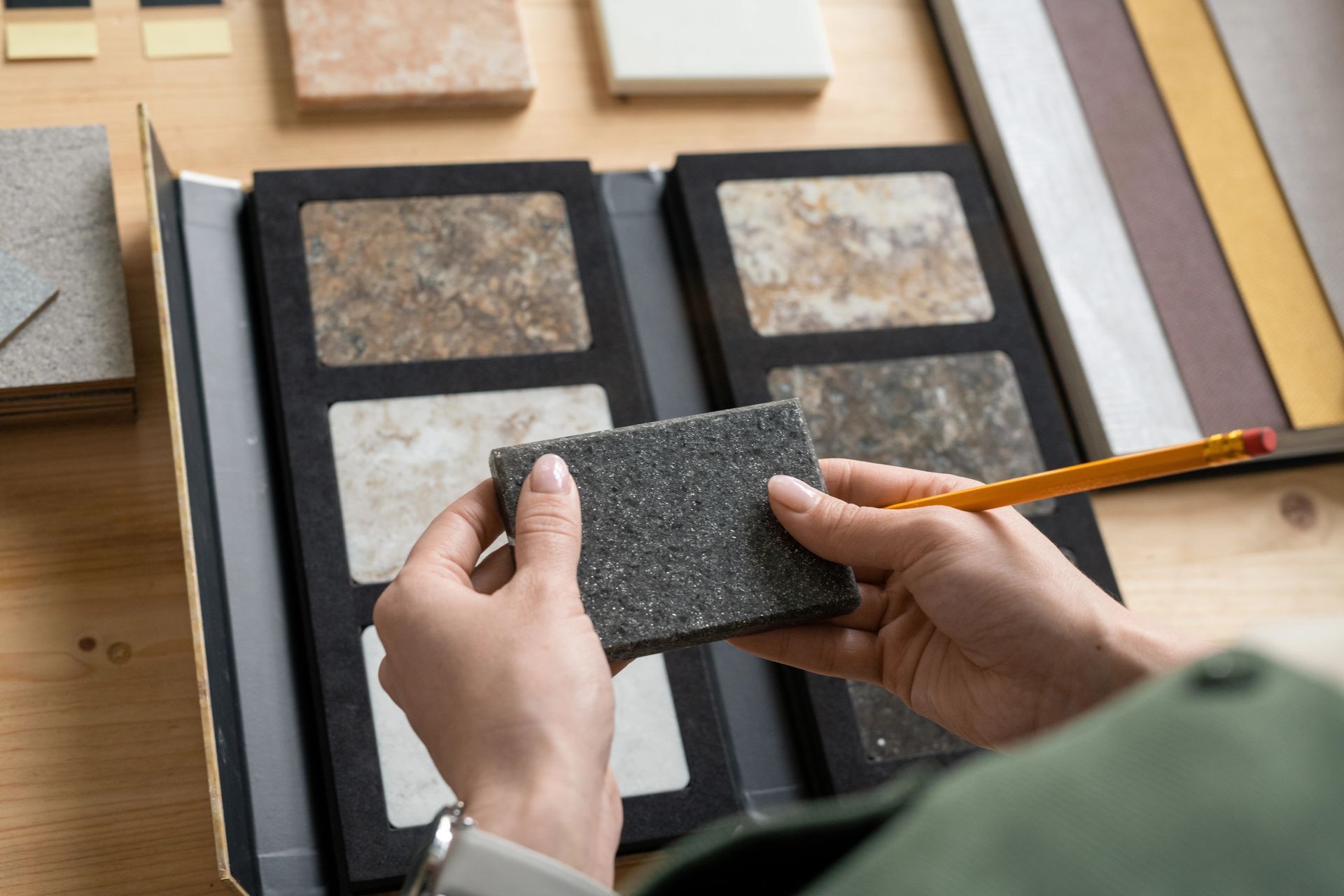 Person holding a dark gray tile, comparing it to other samples in a binder.