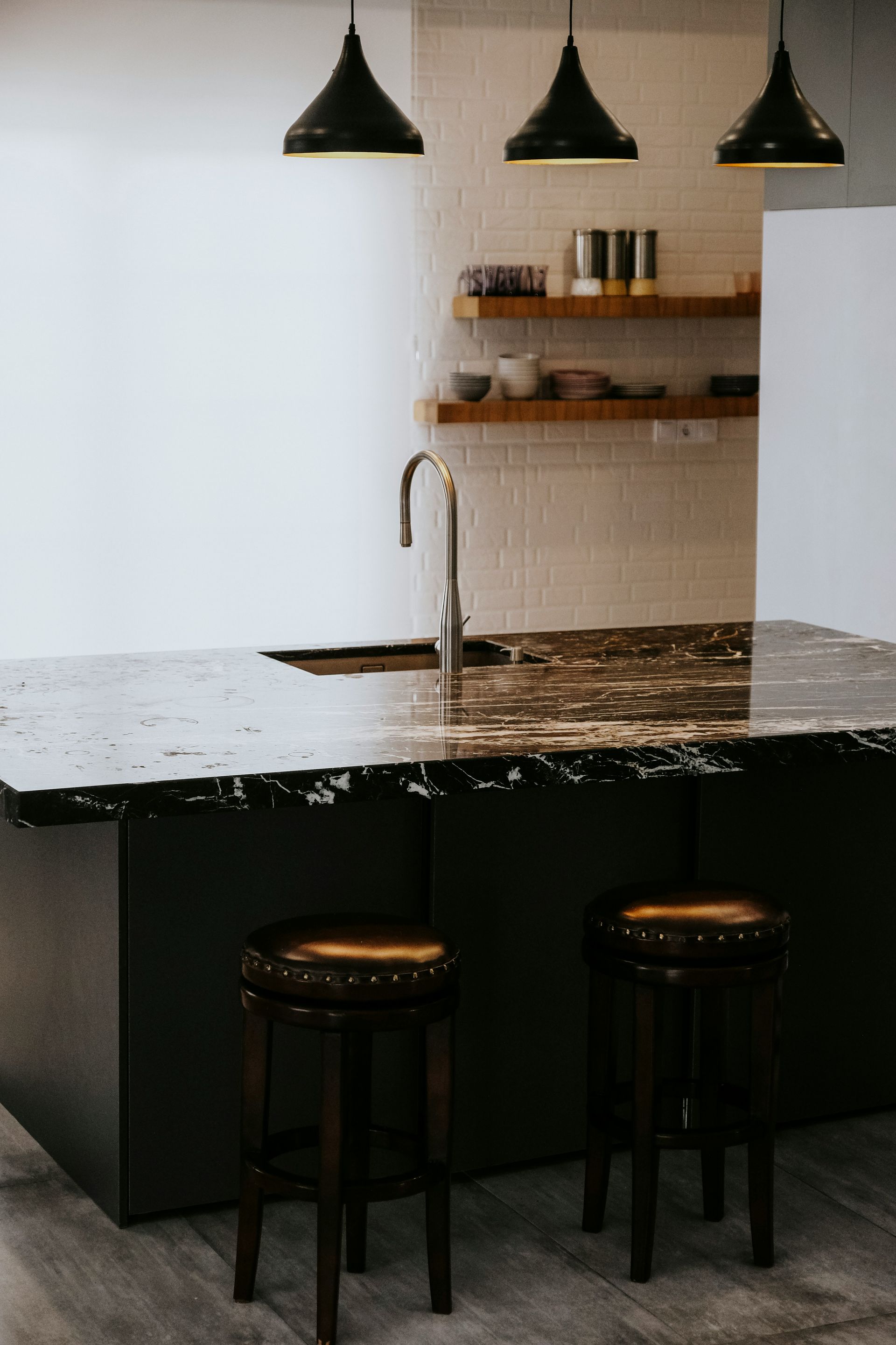 A kitchen with a marble counter top , sink , and stools.