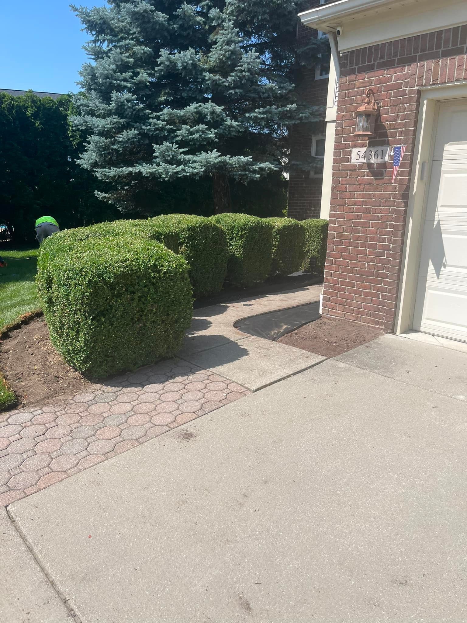 A brick house with a white garage door and bushes in front of it.