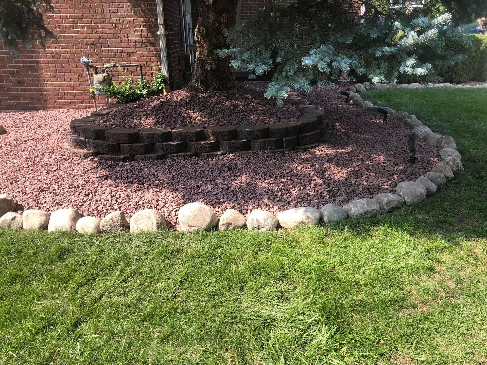 A lawn with a rock border and a brick wall in the background.