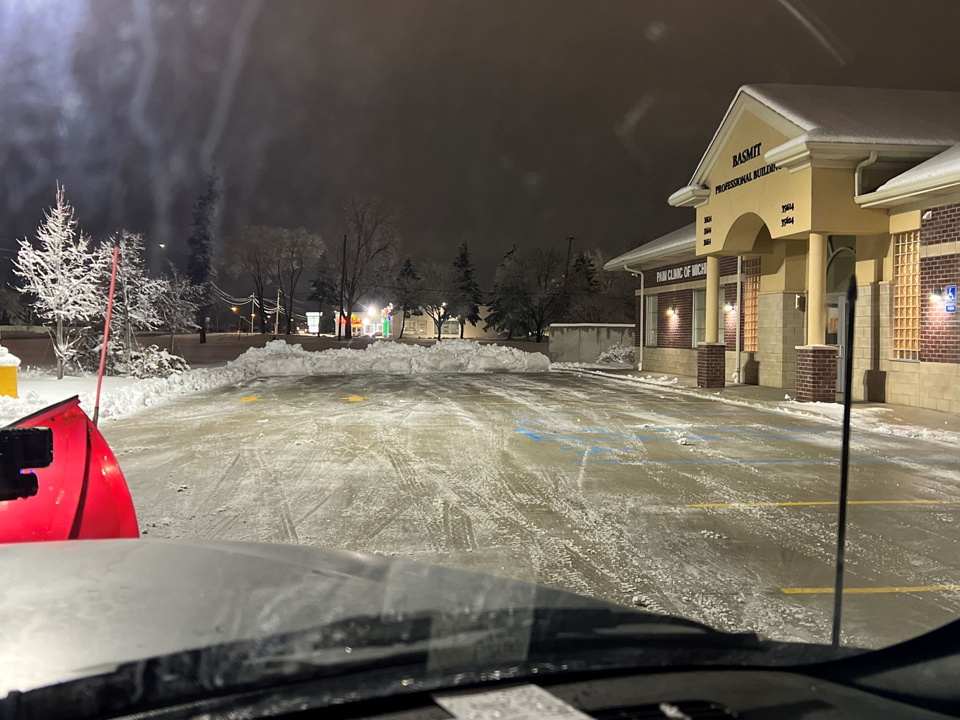 A snow plow is clearing a parking lot at night