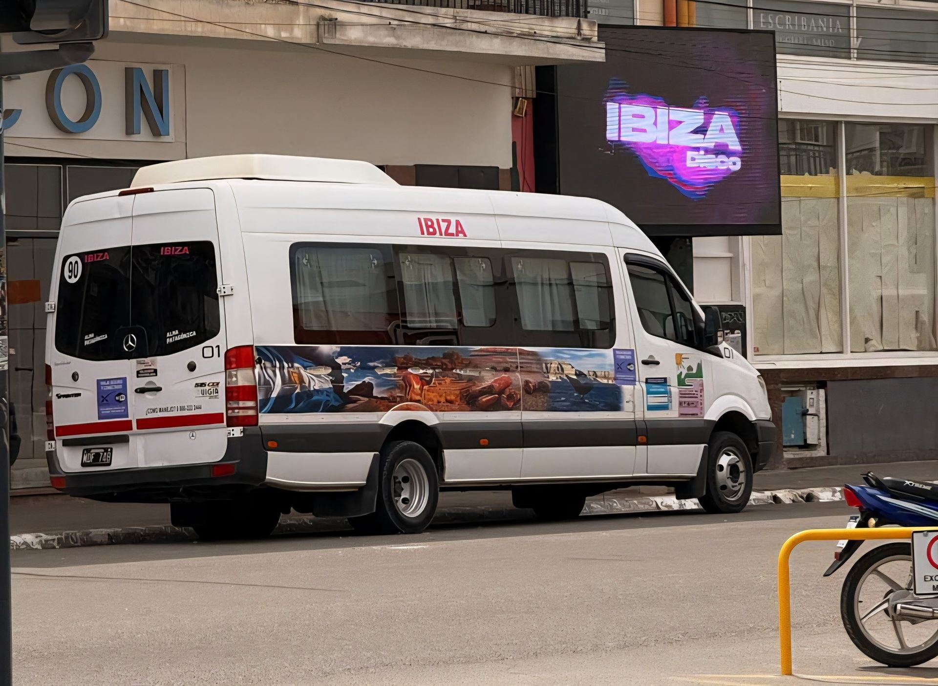 Furgoneta blanca con gráfico lateral colorido estacionada en una calle cerca de un cartel de