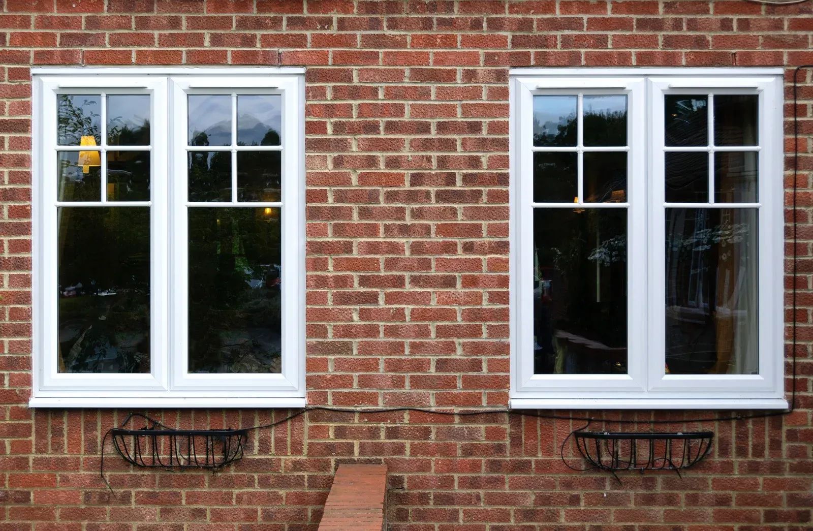 Two white-framed windows on a brick wall, each with a small black planter beneath.