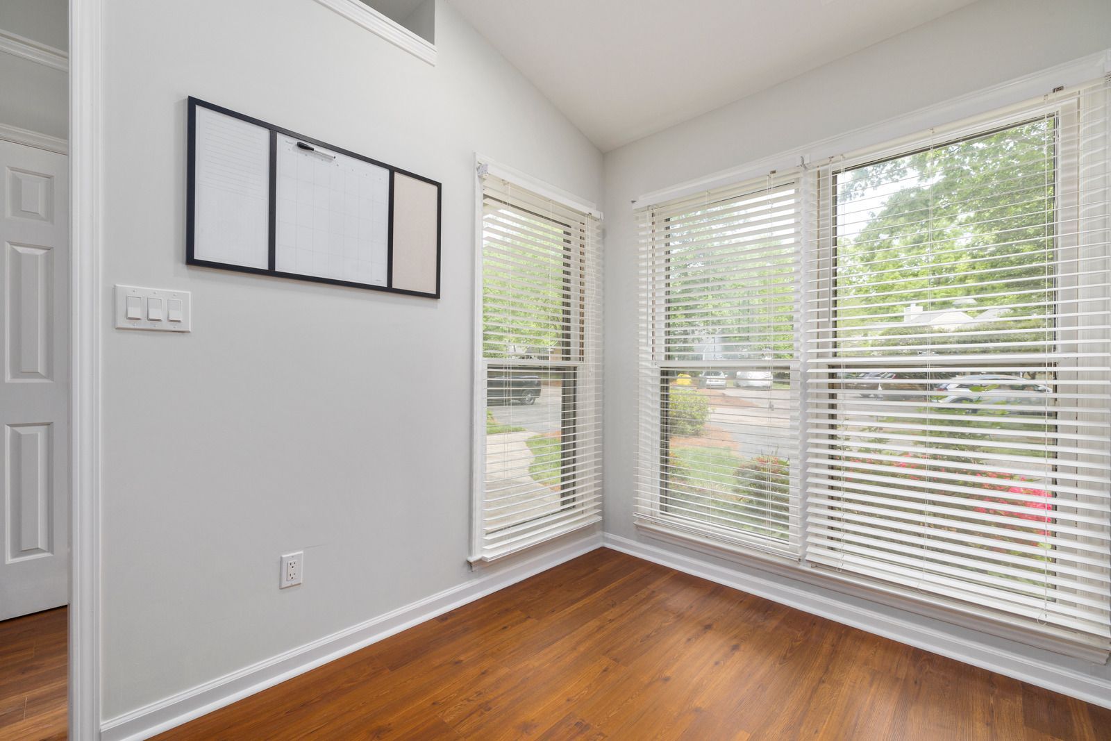 An empty room with hardwood floors and white blinds.