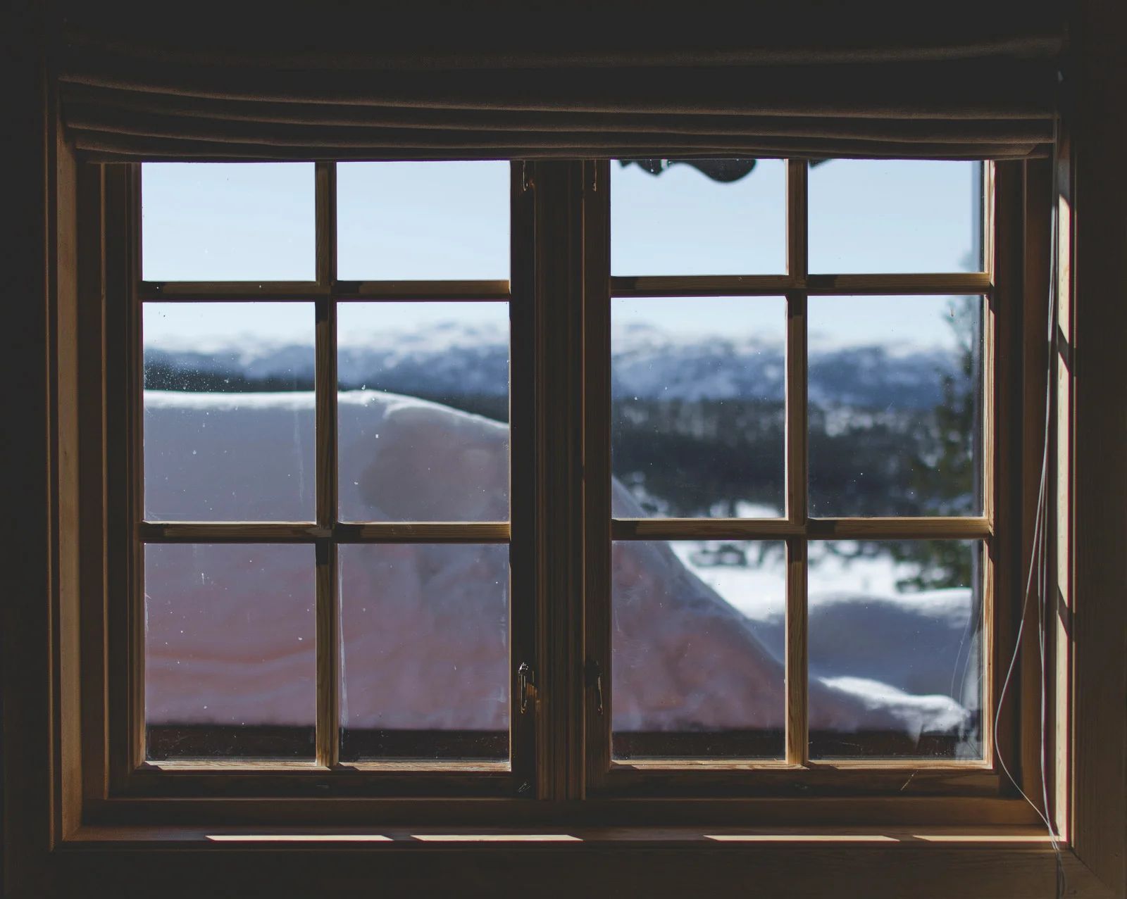 Window overlooking snowy landscape with mountains and blue sky.