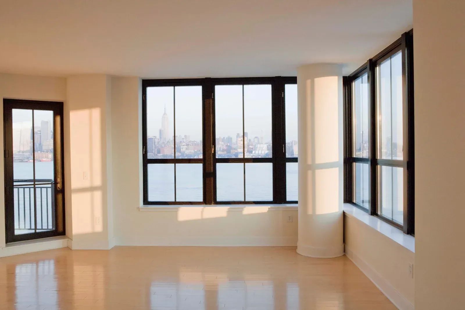Empty room with large windows overlooking a city. Sunlight streams in.