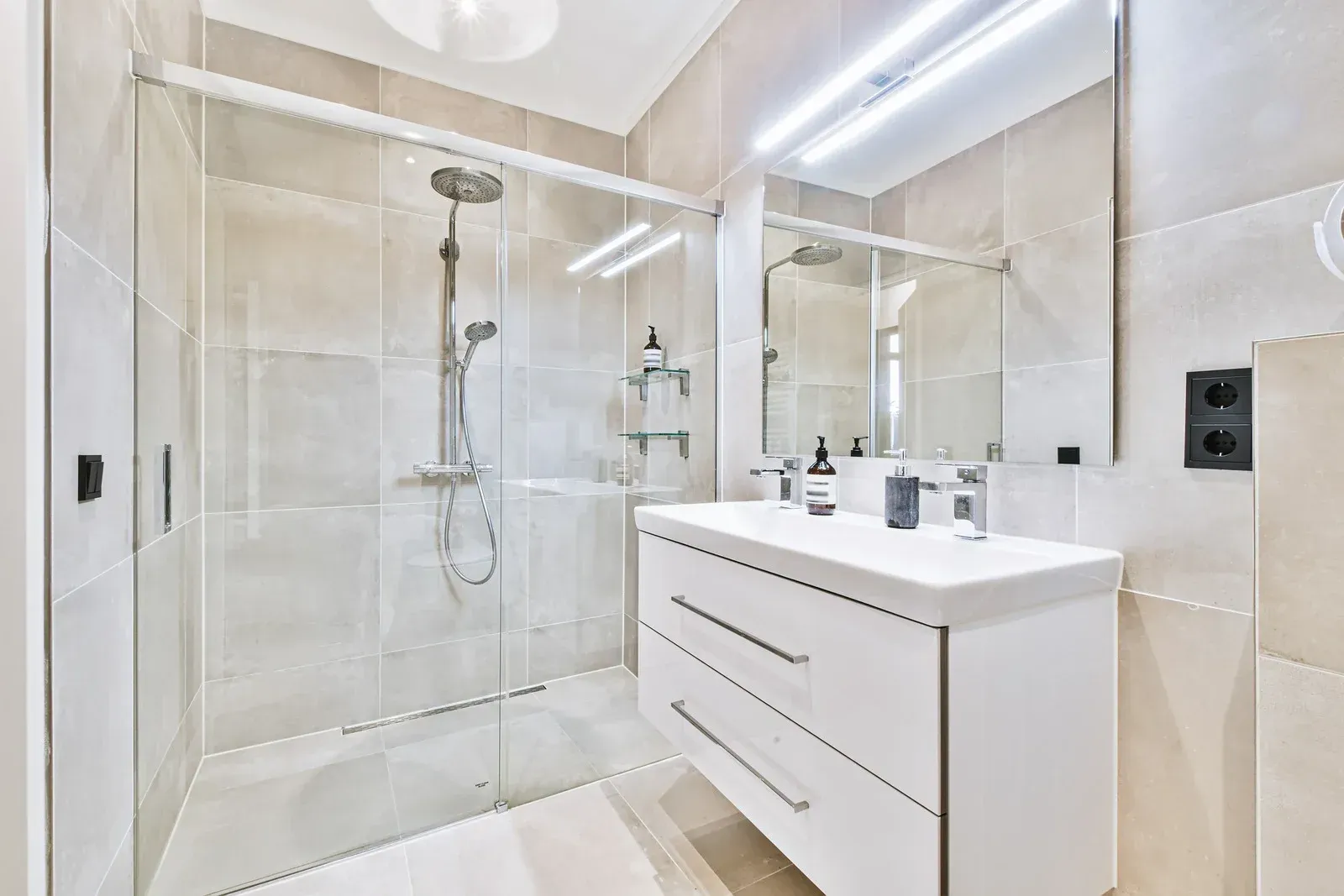 A bathroom with a walk in shower , sink , mirror and vanity.