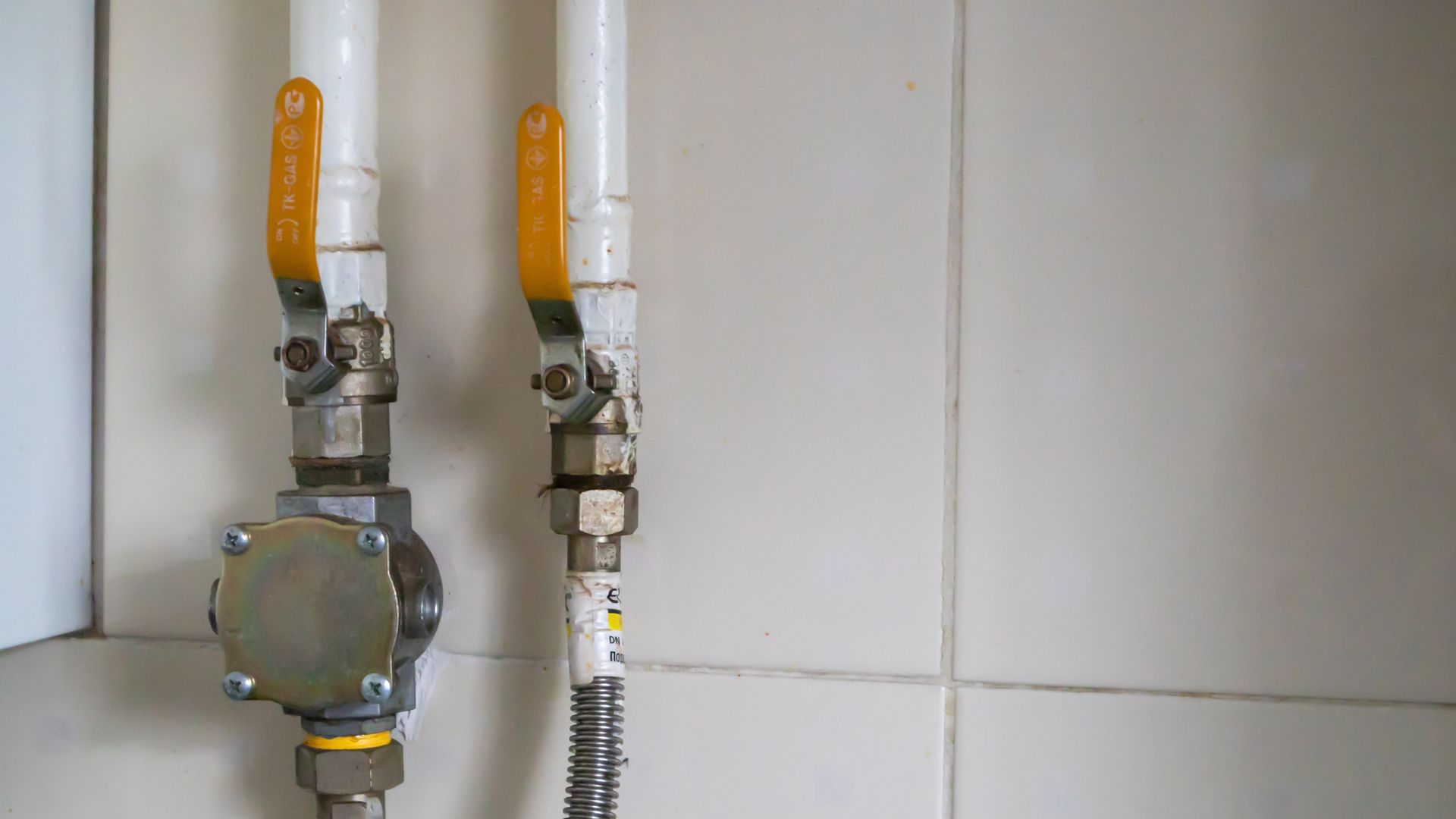 Yellow valves and natural gas pipes in a modern home boiler room in a kitchen with ceramic tiles