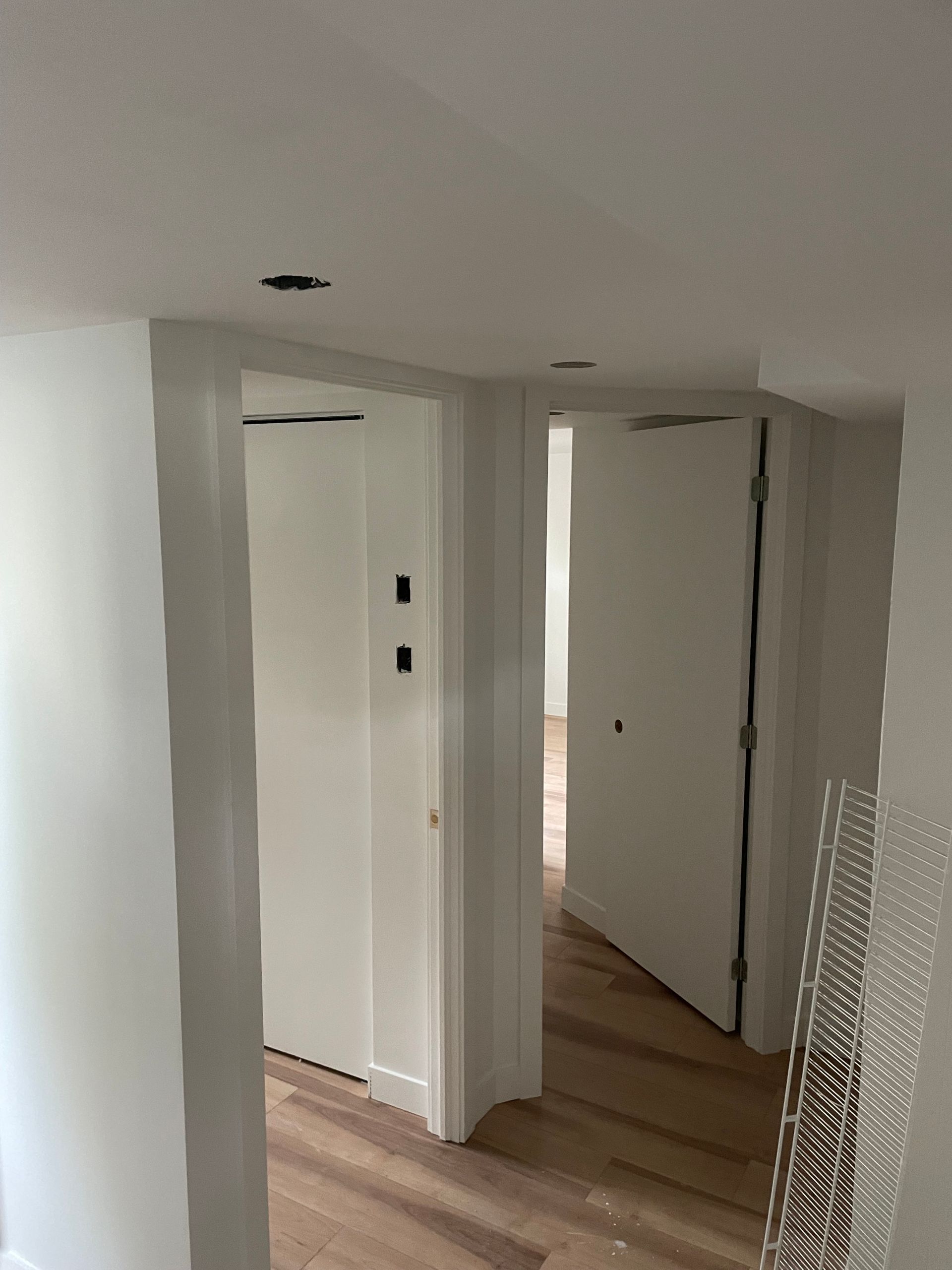 Un couloir aux murs blancs et parquet menant à une pièce.