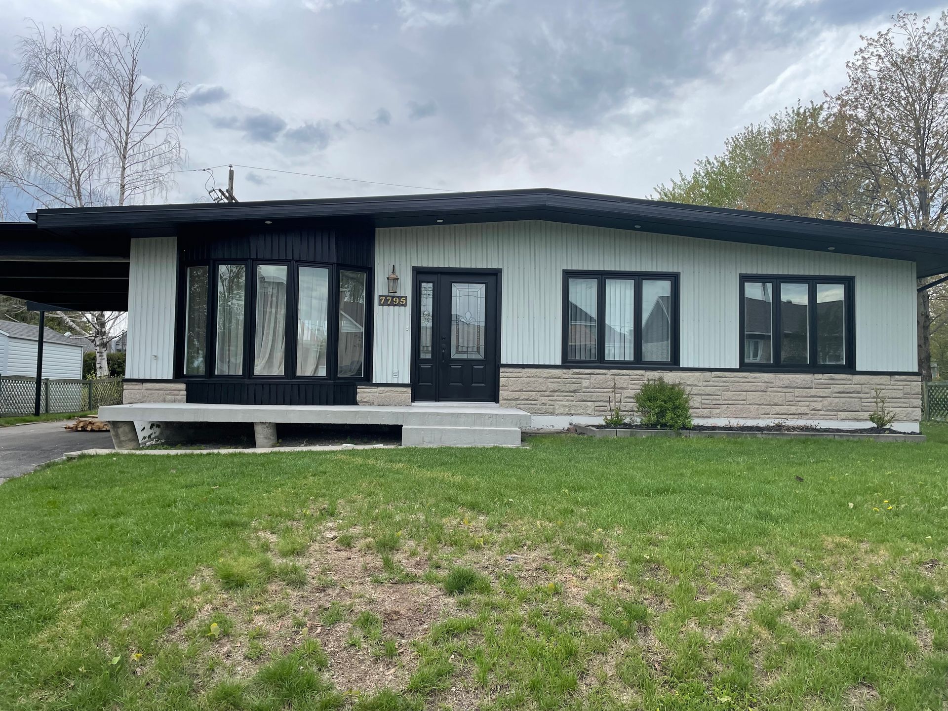 Une maison blanche avec un toit noir se trouve au sommet d'une pelouse verte et luxuriante.