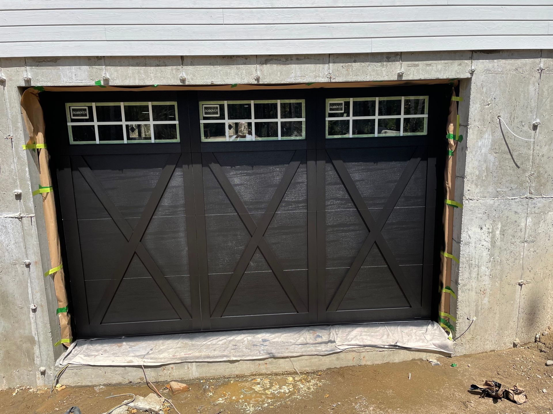 Une porte de garage noire est en cours d'installation au sous-sol d'une maison.