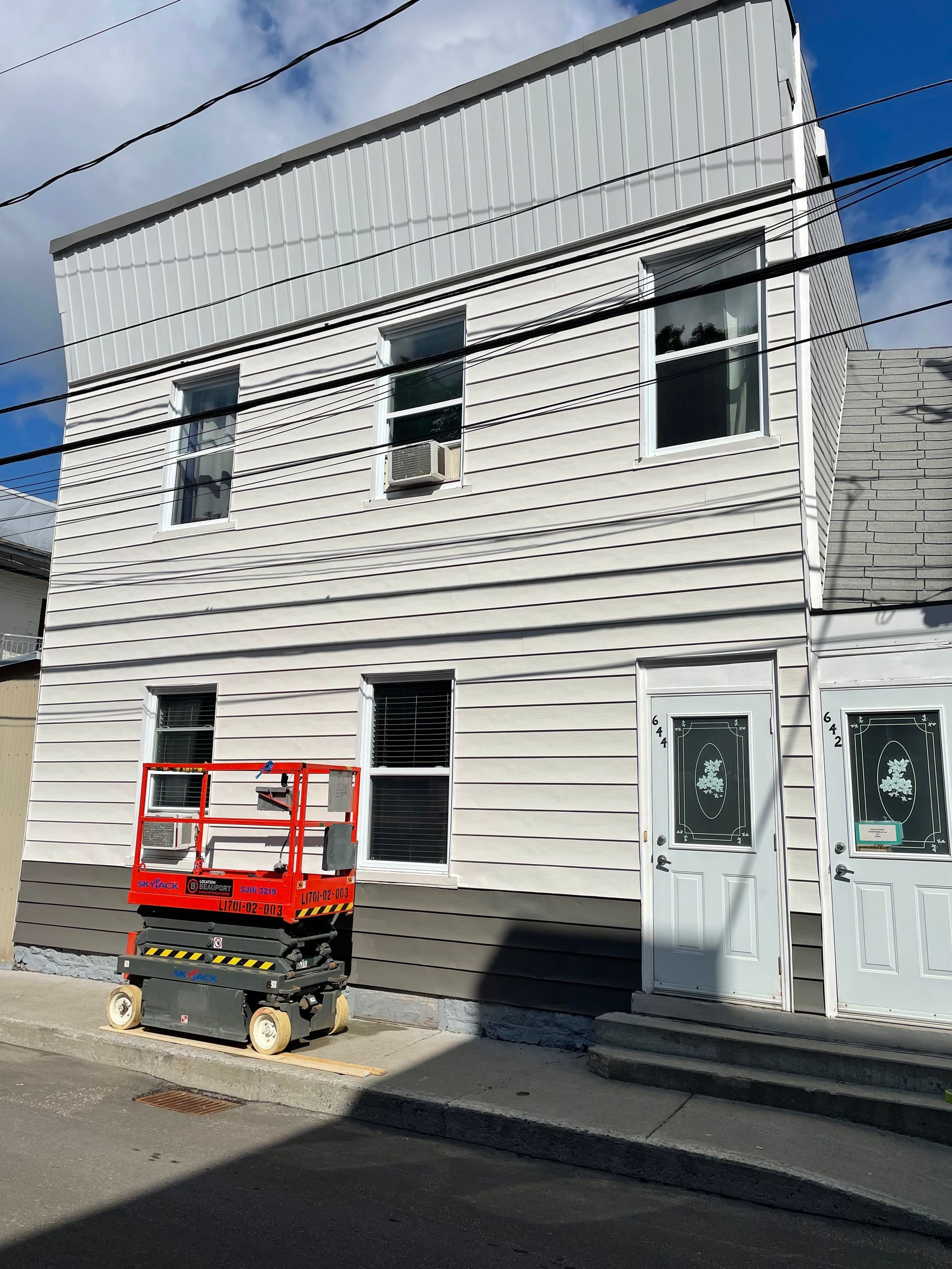 Un ascenseur à ciseaux rouge est garé devant un immeuble.
