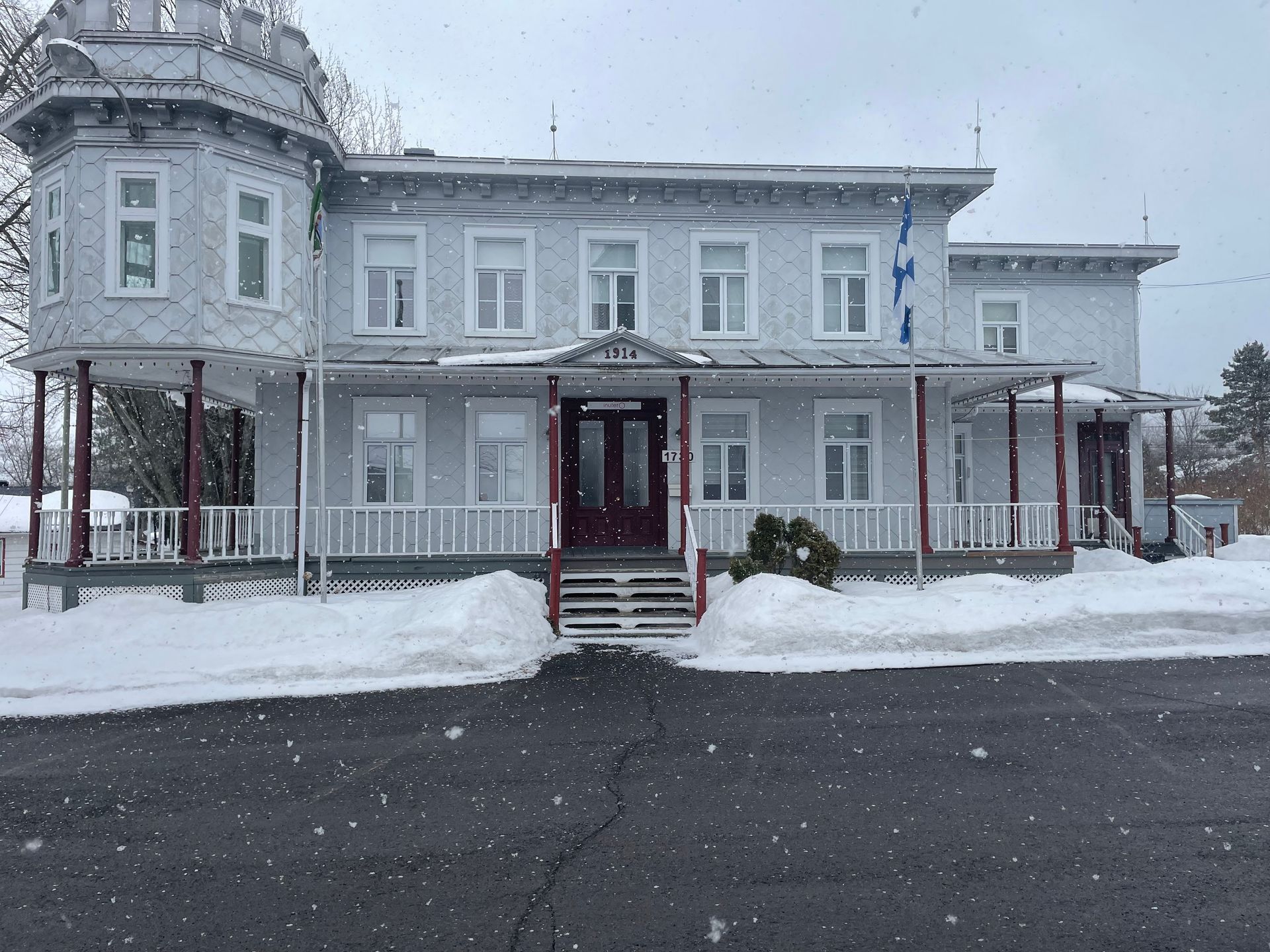 Bâtiment victorien gris avec porche, marches et terrain enneigés, sous un ciel d'ébène.