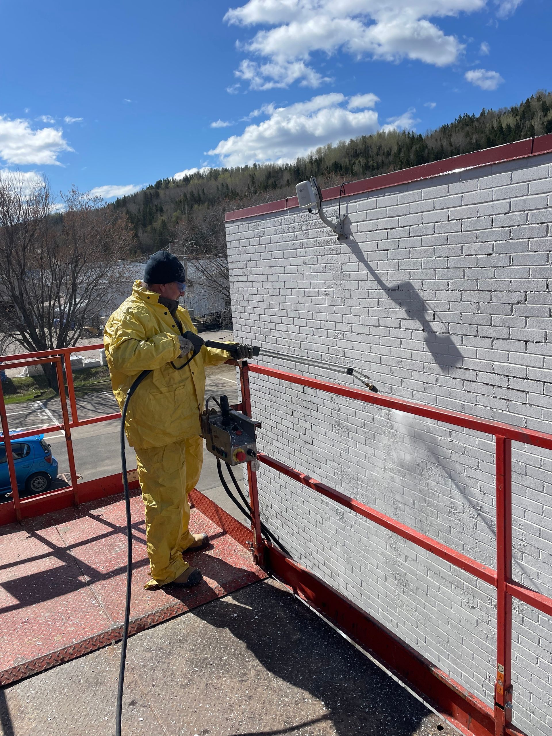 Un homme en costume jaune nettoie un mur de briques blanches avec un nettoyeur haute pression.
