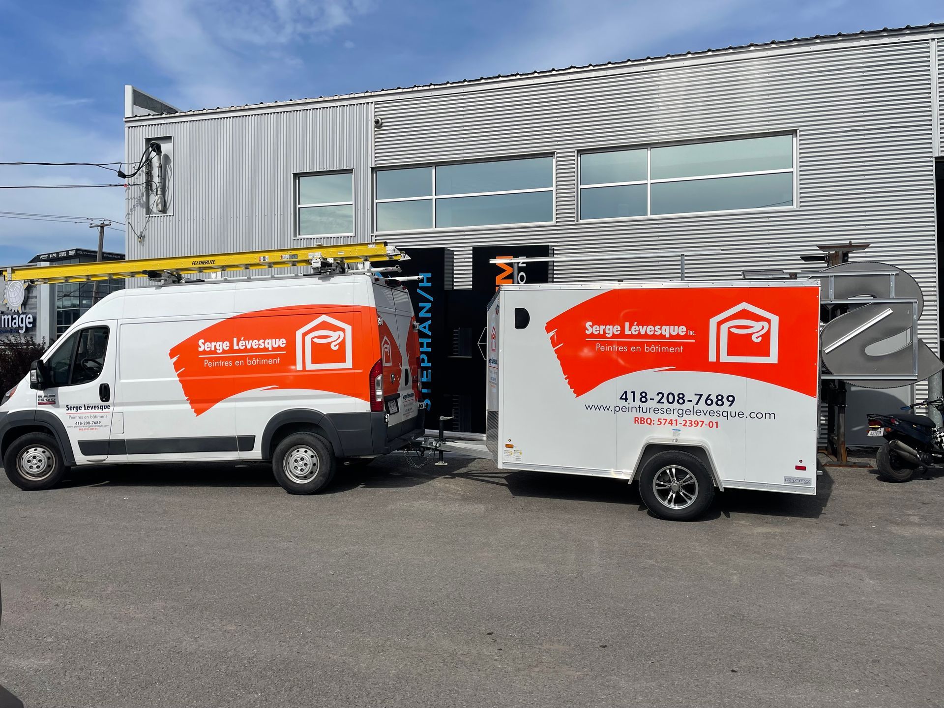 Fourgonnette blanche et remorque avec logo orange stationnées devant un bâtiment.